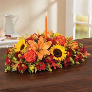 Autumn Celebration Arrangement Warm homes and hearts throughout the fall season with this amazing centerpiece. Enjoy the views of orange roses, sunflowers, red daisy poms, orange lilies, orange mini carnations, and accents of solidago, dried oak leaves, and salal.