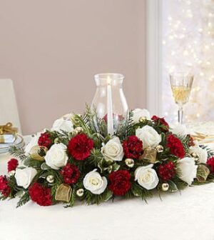 The Exquisite Christmas Cheer Centerpiece is perfectly arranged to suit the holiday festivities and bring about Christmas cheer. Red and white roses are arranged among evergreen furnishings & golden accents to create a graceful centerpiece that can accommodate any Christmas event. An elegant candle in the center is surrounded by a glass vase finishes this centerpiece, bringing radiance to the holiday atmosphere.